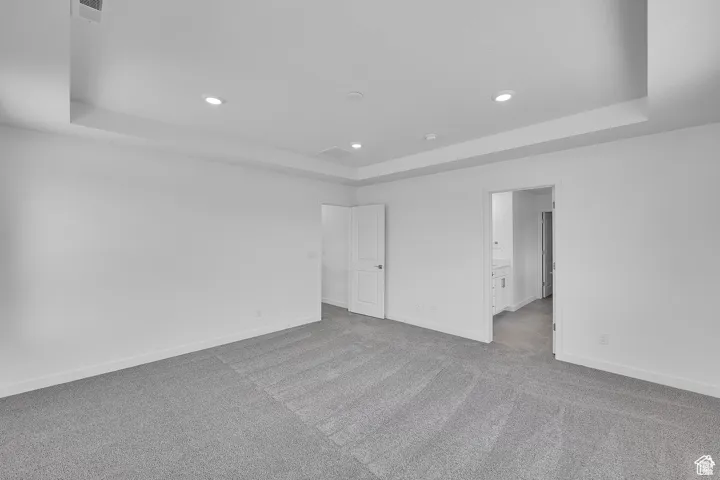 Spare room featuring a tray ceiling, light colored carpet, and recessed lighting