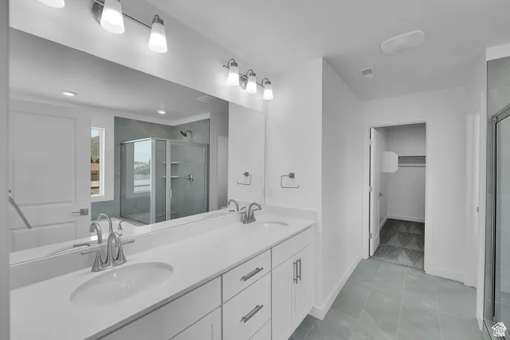 Bathroom featuring a shower stall, double vanity, light tile patterned floors, and a spacious closet