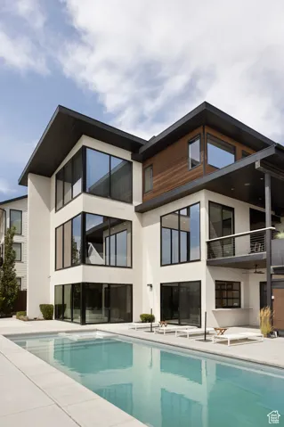 Rear view of house featuring an outdoor pool, stucco siding, a balcony, and a patio