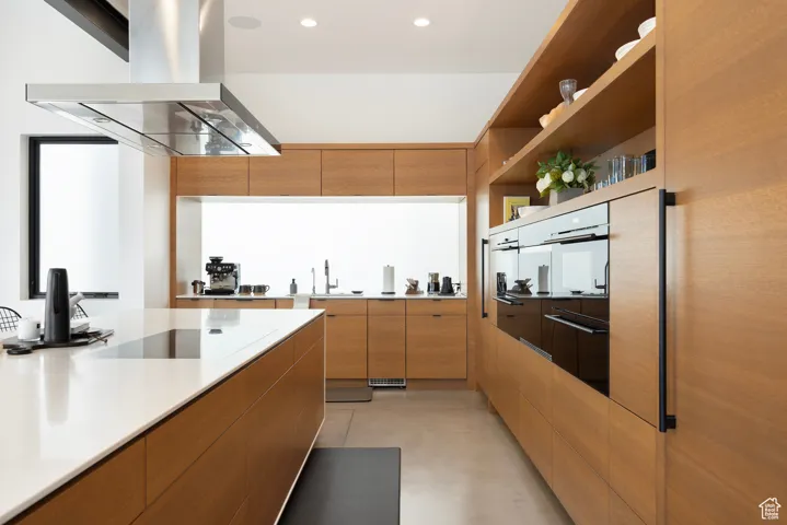 Kitchen featuring modern cabinets, island exhaust hood, a warming drawer, recessed lighting, and brown cabinetry
