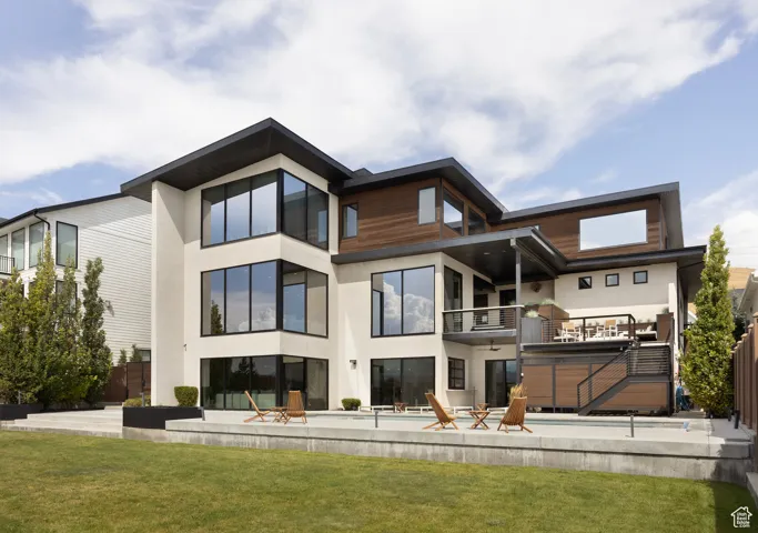 Back of house with a yard, stucco siding, a balcony, and a patio