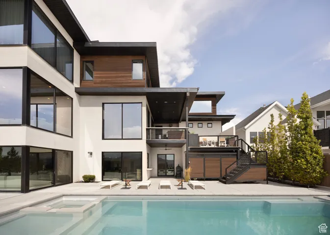 Back of house with stairway, stucco siding, a balcony, and a pool with connected hot tub