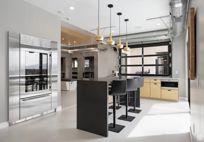 Kitchen featuring modern cabinets, a breakfast bar, stainless steel built in refrigerator, concrete flooring, and dark countertops