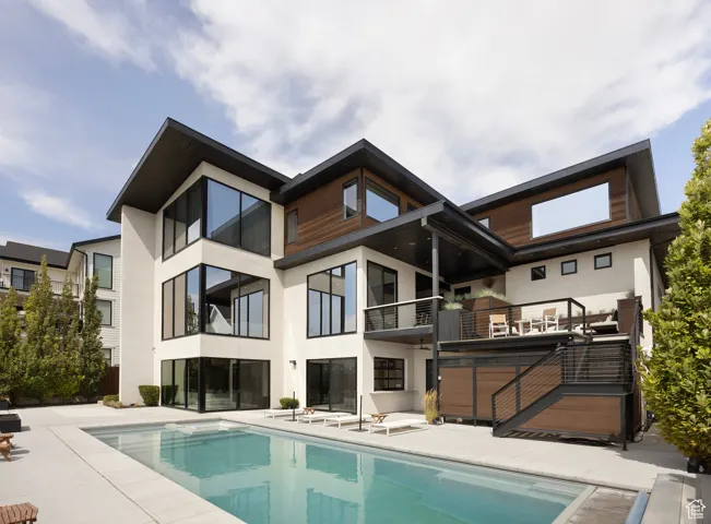Rear view of property featuring stucco siding, an outdoor pool, and a balcony