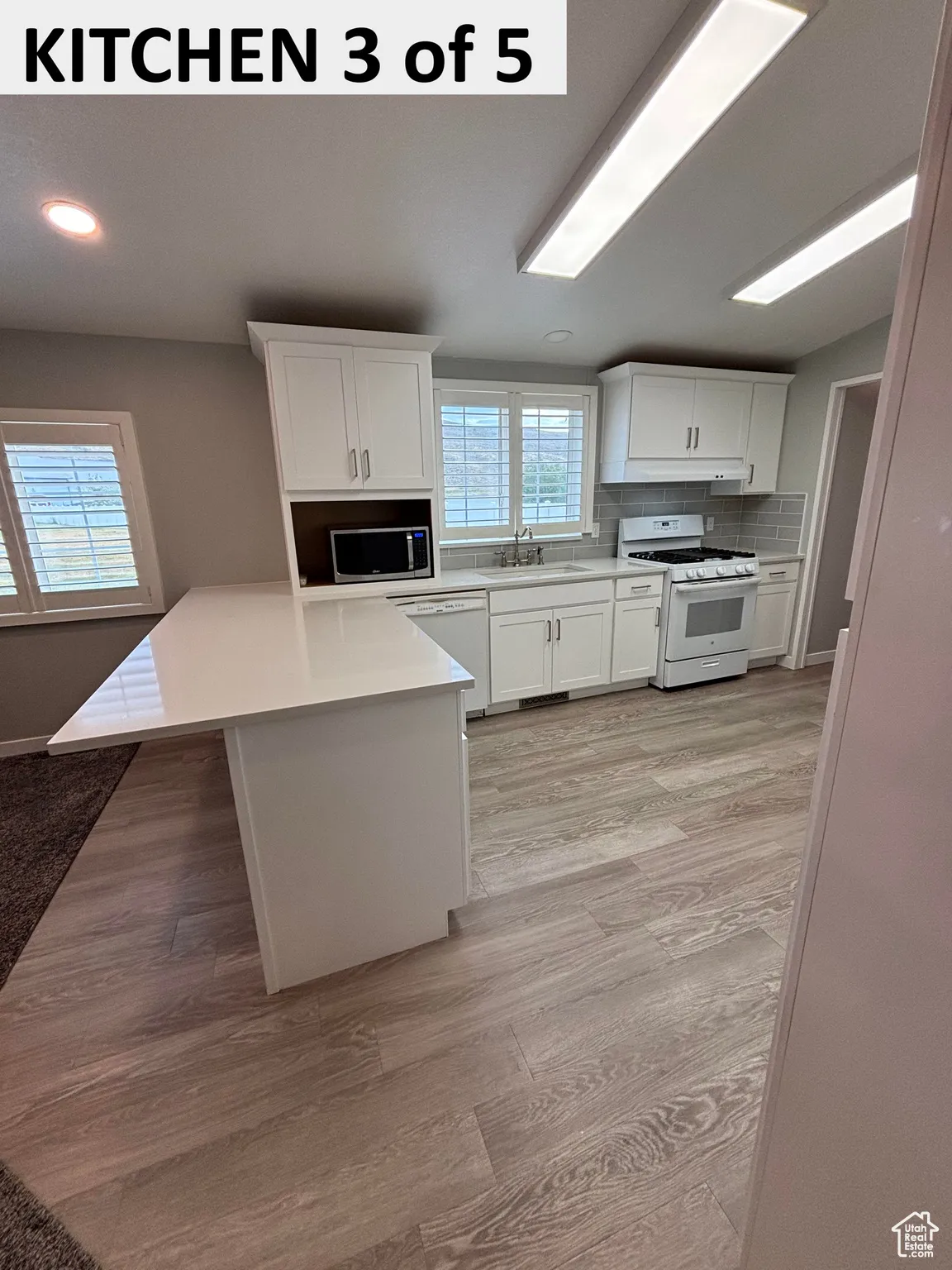 Kitchen featuring white cabinetry, decorative backsplash, white appliances, a peninsula, and light wood-style LVP floors