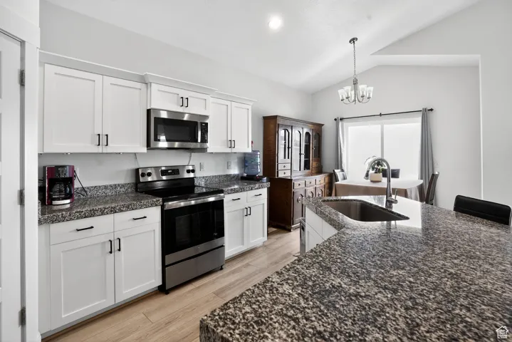 Kitchen featuring stainless steel appliances, pendant lighting, white cabinetry, lofted ceiling, and light wood-style flooring