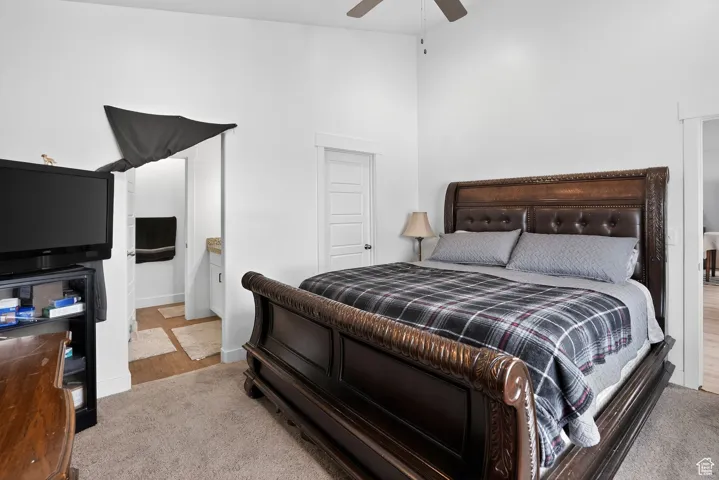 Bedroom featuring ensuite bath, a high ceiling, ceiling fan, and light wood-style flooring