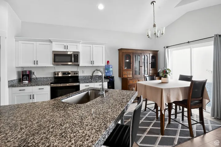 Kitchen with white cabinets, stainless steel appliances, dark stone counters, decorative light fixtures, and a chandelier