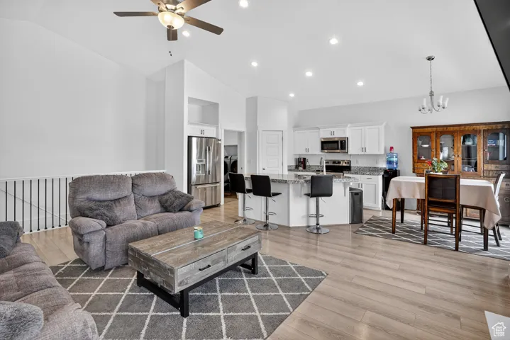 Living area with light wood-type flooring, a chandelier, a ceiling fan, recessed lighting, and high vaulted ceiling