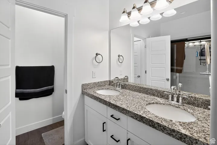 Full bath with double vanity, dark wood-type flooring, and a shower with shower door