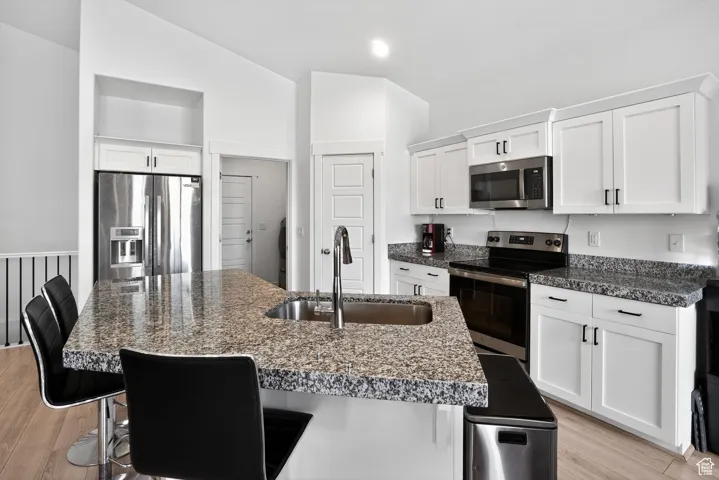 Kitchen with a breakfast bar area, appliances with stainless steel finishes, white cabinetry, light wood finished floors, and vaulted ceiling