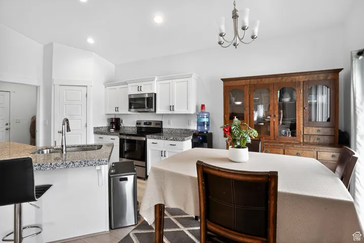 Kitchen featuring white cabinetry, appliances with stainless steel finishes, a chandelier, light wood-type flooring, and a breakfast bar