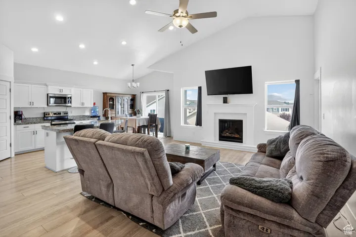 Living area with high vaulted ceiling, light wood-style flooring, recessed lighting, a ceiling fan, and a glass covered fireplace