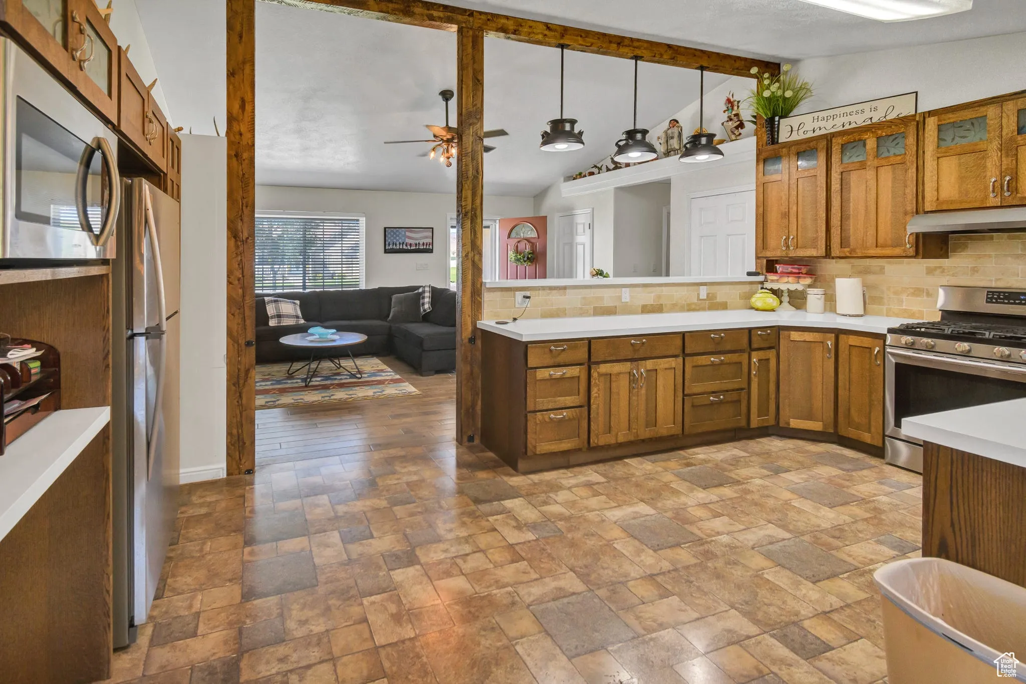 Kitchen with glass insert cabinets, brown cabinetry, stainless steel appliances, tasteful backsplash, and light countertops