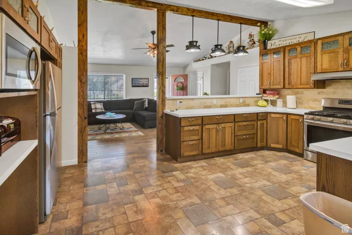 Kitchen with glass insert cabinets, brown cabinetry, stainless steel appliances, tasteful backsplash, and light countertops