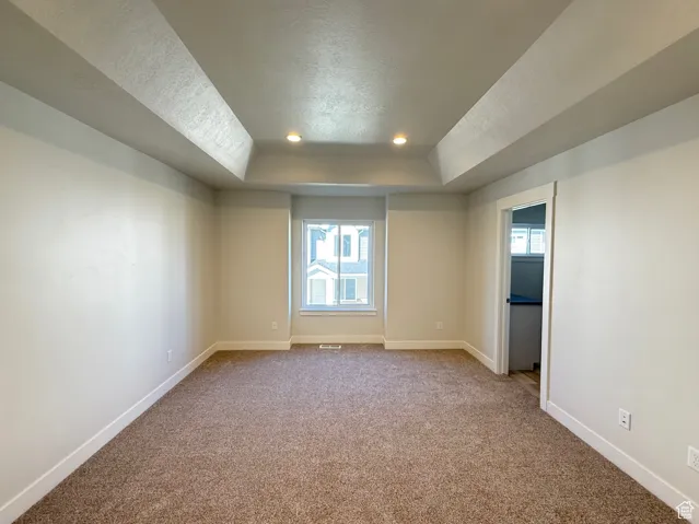 Primary bedroom featuring light colored carpet, healthy amount of natural light, a tray ceiling, a textured ceiling, and recessed lighting