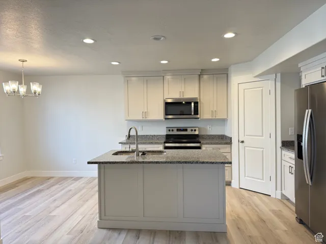 Kitchen with appliances with stainless steel finishes, dark stone counters, recessed lighting, light wood-type flooring, and a center island with sink