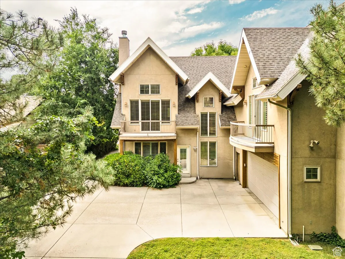 Rear view of property featuring a balcony, a chimney, roof with shingles, stucco siding, and concrete driveway