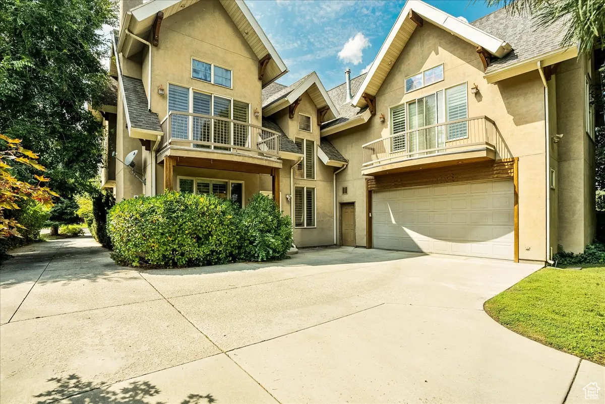 View of front facade featuring a balcony, concrete driveway, stucco siding, an attached garage, and a shingled roof