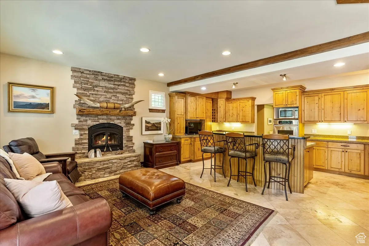 Living room with beamed ceiling, recessed lighting, and a stone fireplace