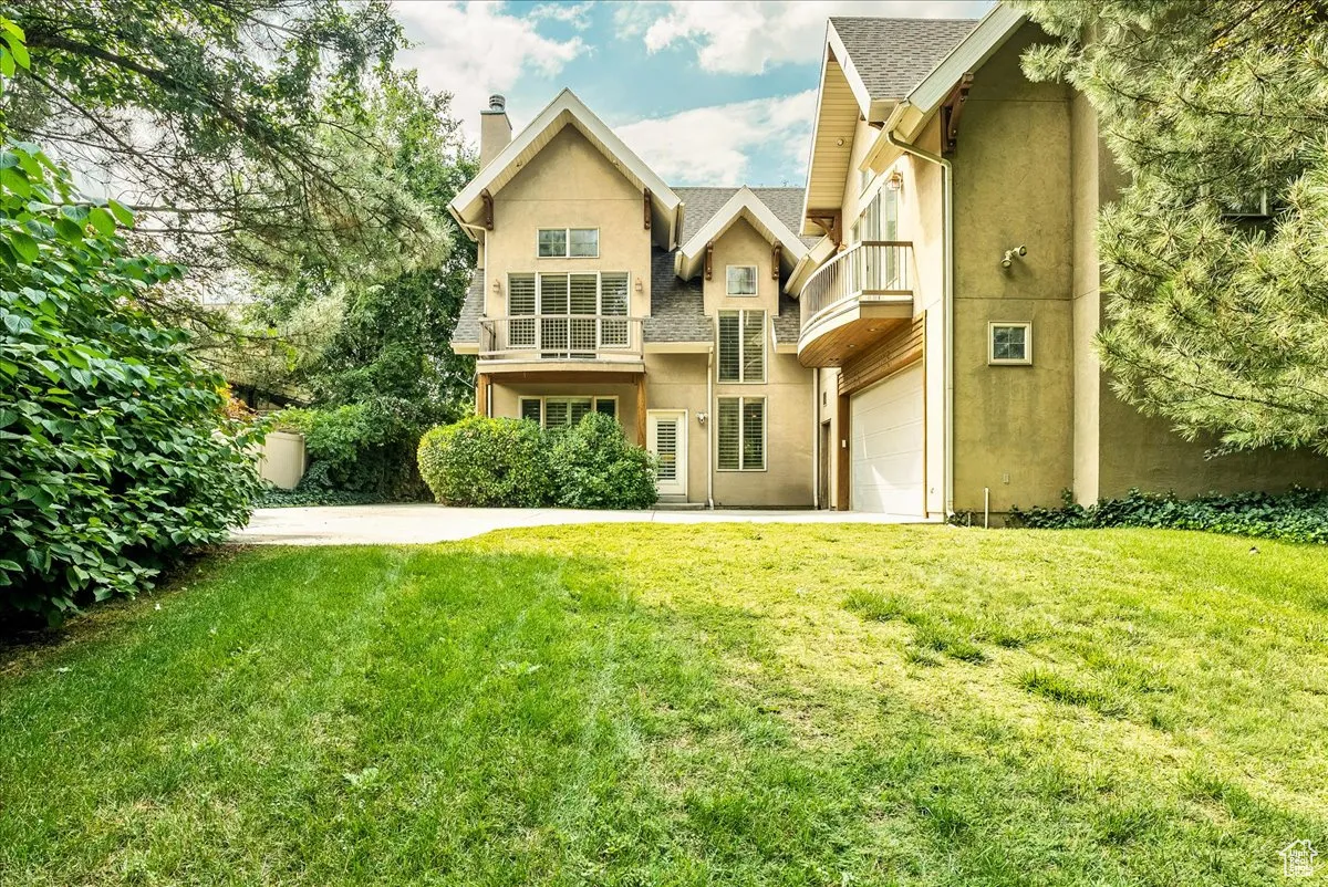 View of front of home featuring a balcony, a front yard, stucco siding, and a chimney