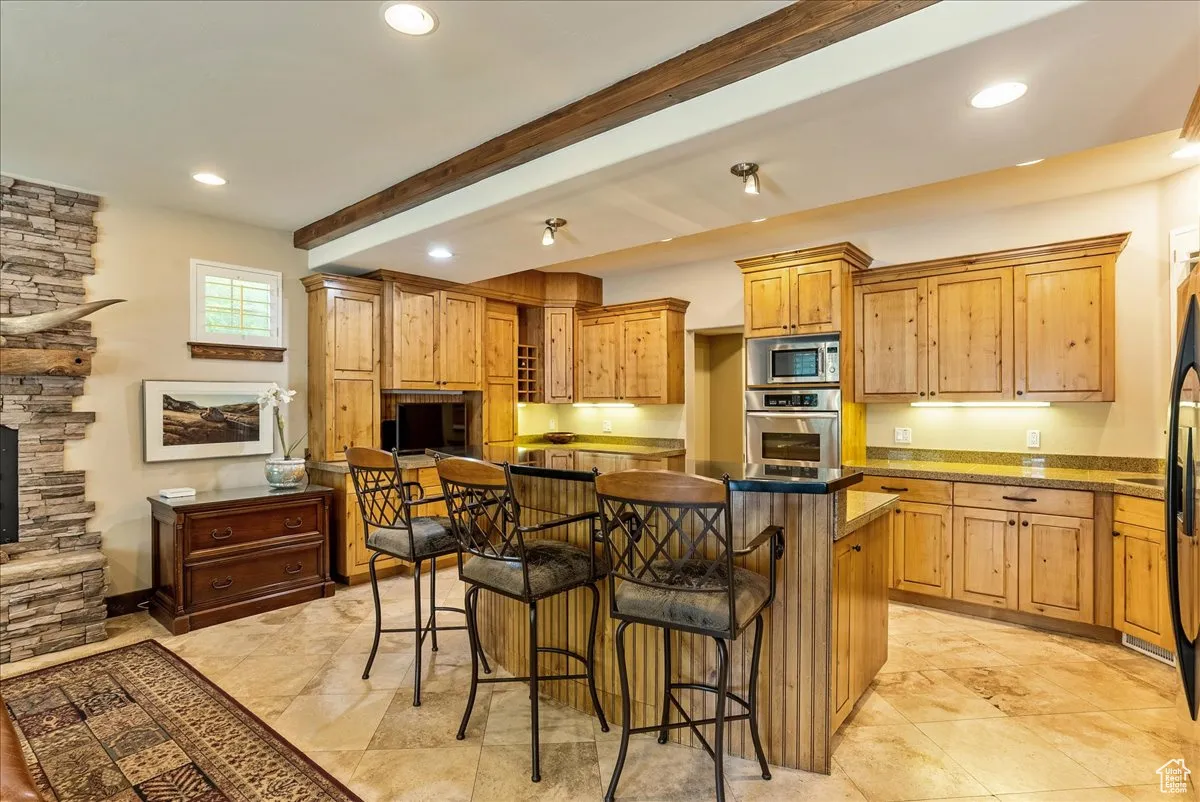 Kitchen featuring a kitchen bar, beam ceiling, a fireplace, appliances with stainless steel finishes, and recessed lighting