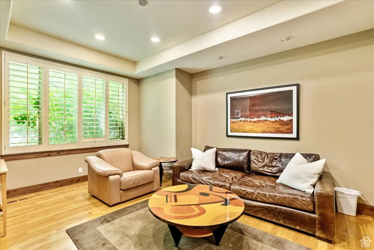 Living area with light wood-type flooring, a raised ceiling, and recessed lighting