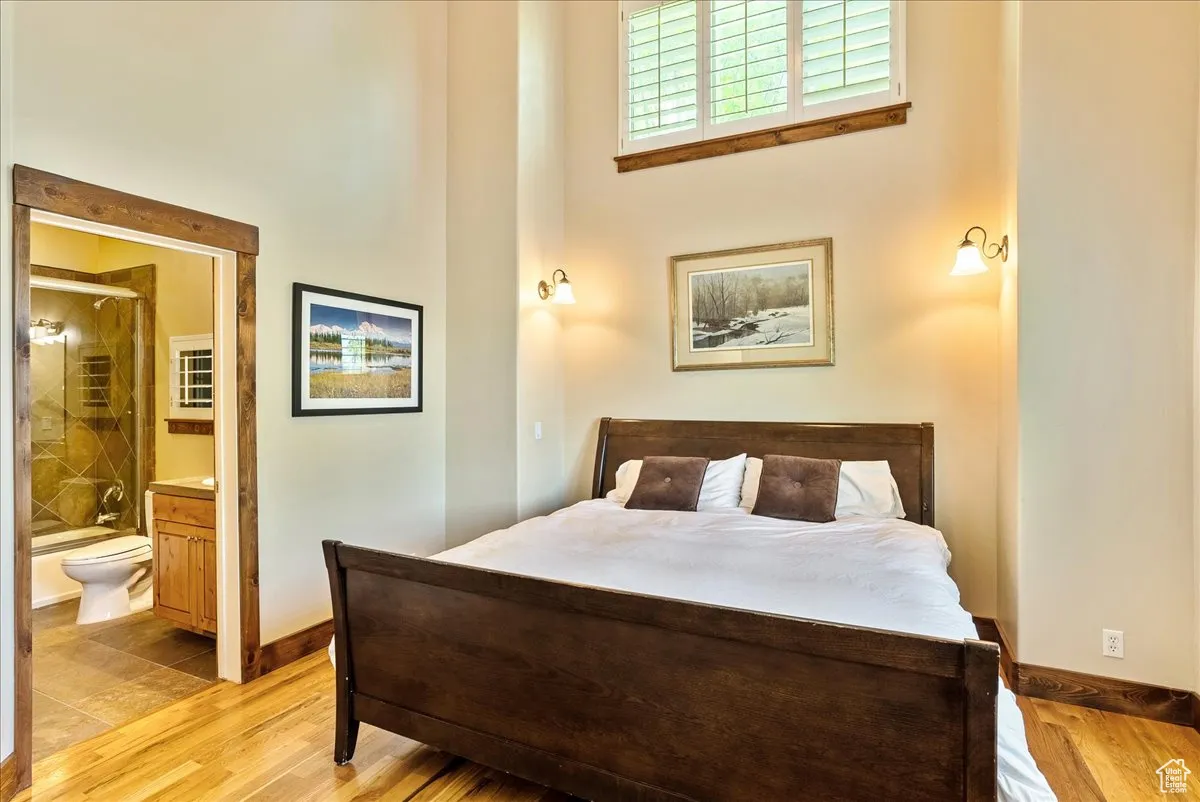 Bedroom featuring wood finished floors, ensuite bath, and a high ceiling