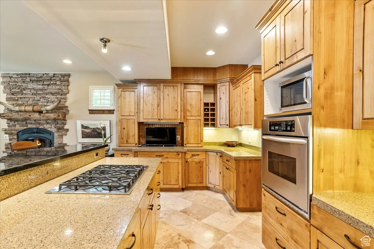 Kitchen with a fireplace, stainless steel appliances, recessed lighting, and light stone counters