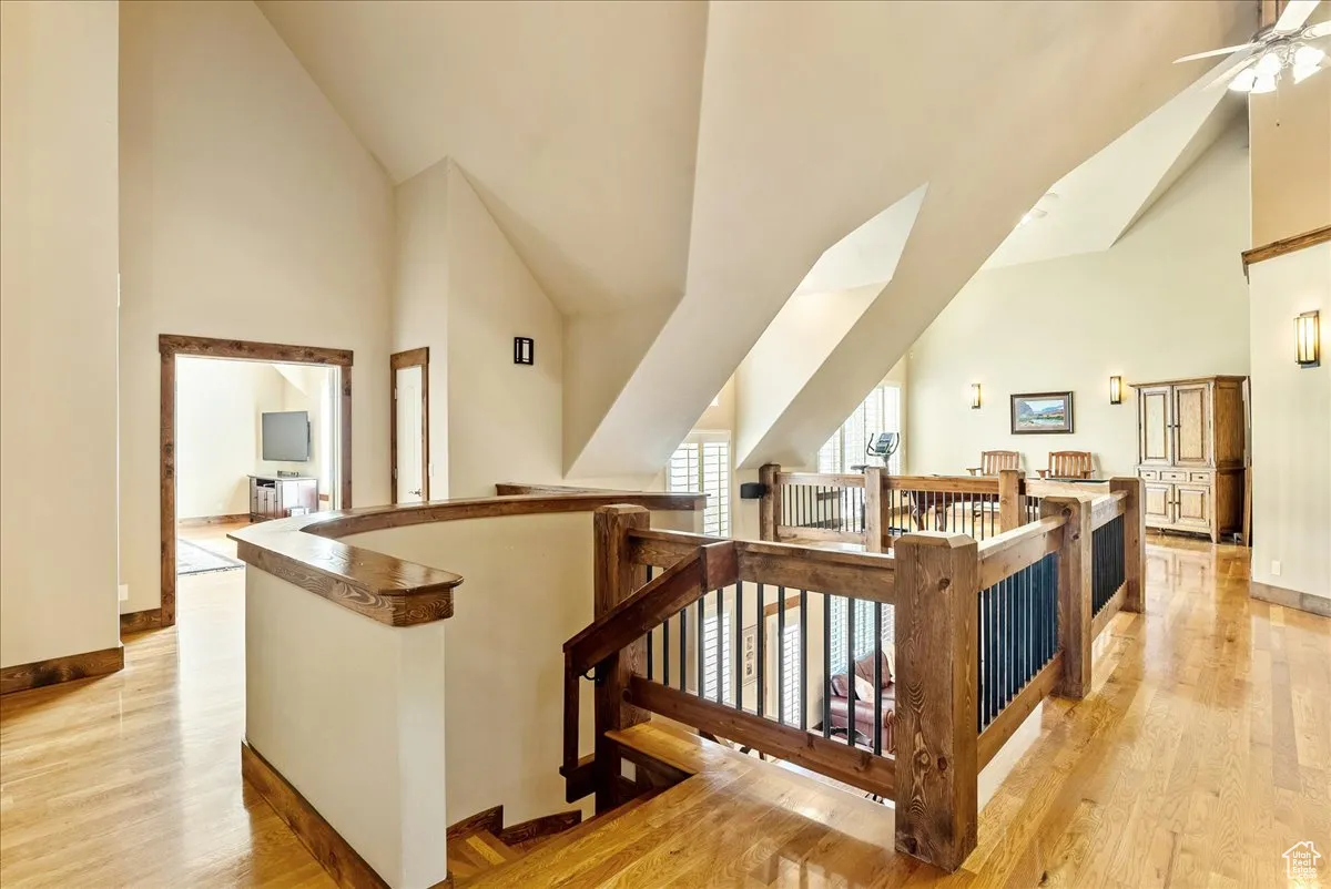 Stairs with high vaulted ceiling, wood finished floors, and a ceiling fan