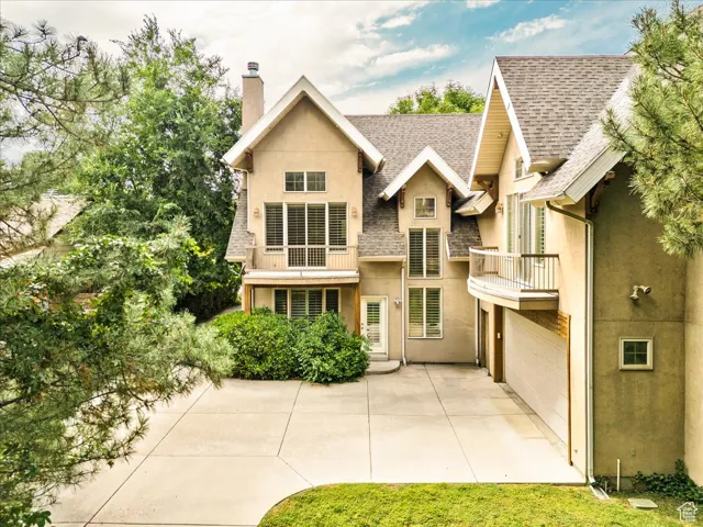 Rear view of property featuring a balcony, a chimney, roof with shingles, stucco siding, and concrete driveway