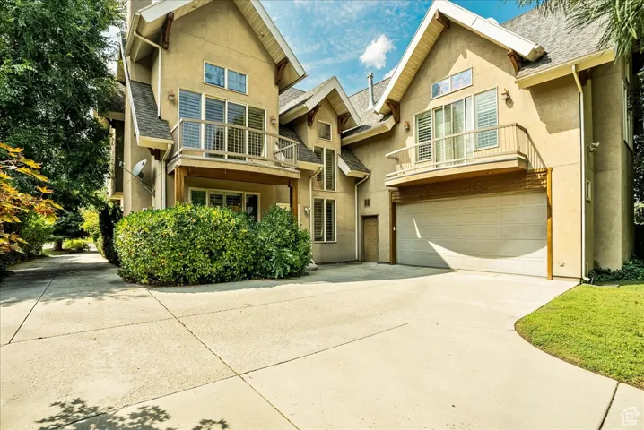 View of front facade featuring a balcony, concrete driveway, stucco siding, an attached garage, and a shingled roof