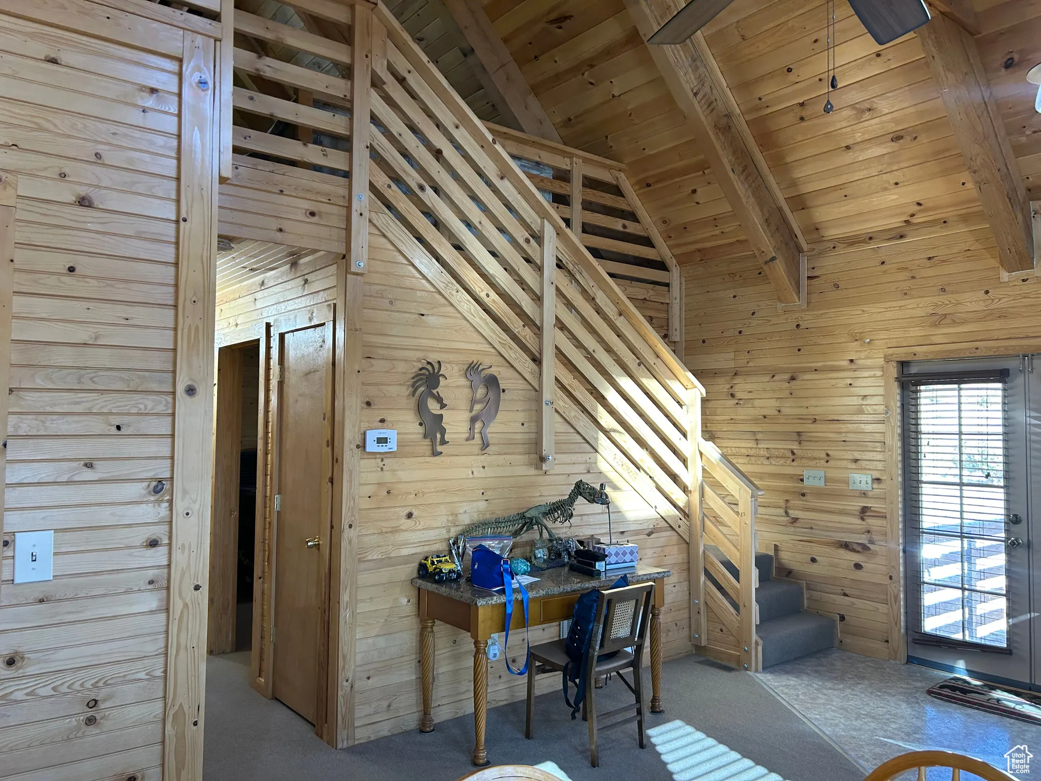 Carpeted office with wooden walls, a wood ceiling with exposed beams, and high vaulted ceiling