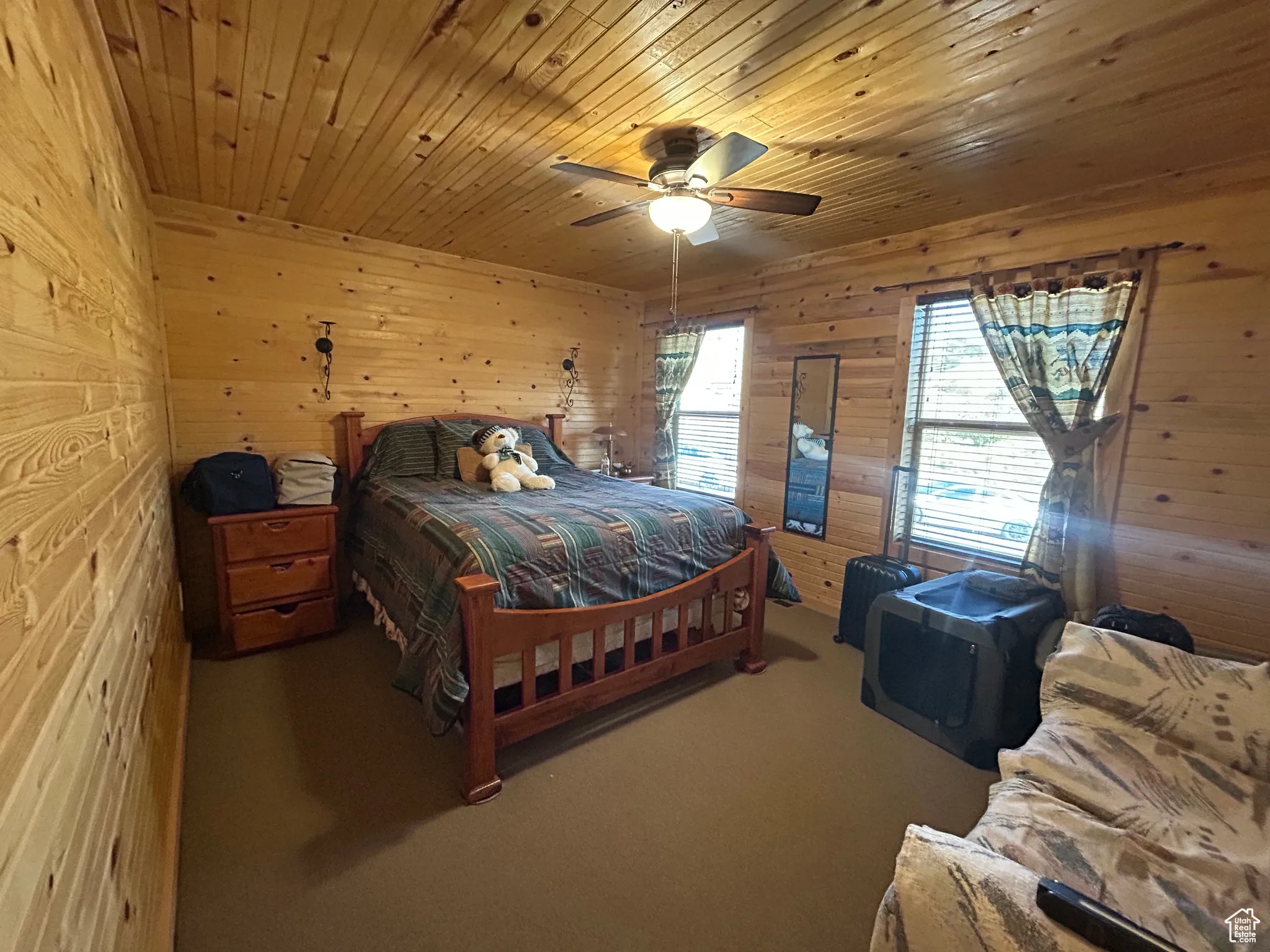 Carpeted bedroom featuring wood walls, wooden ceiling, and ceiling fan