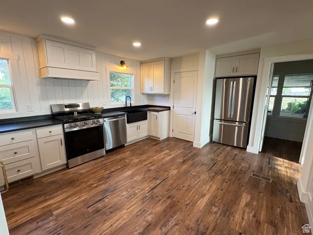 Kitchen with appliances with stainless steel finishes, dark wood-style flooring, custom exhaust hood, dark countertops, and recessed lighting