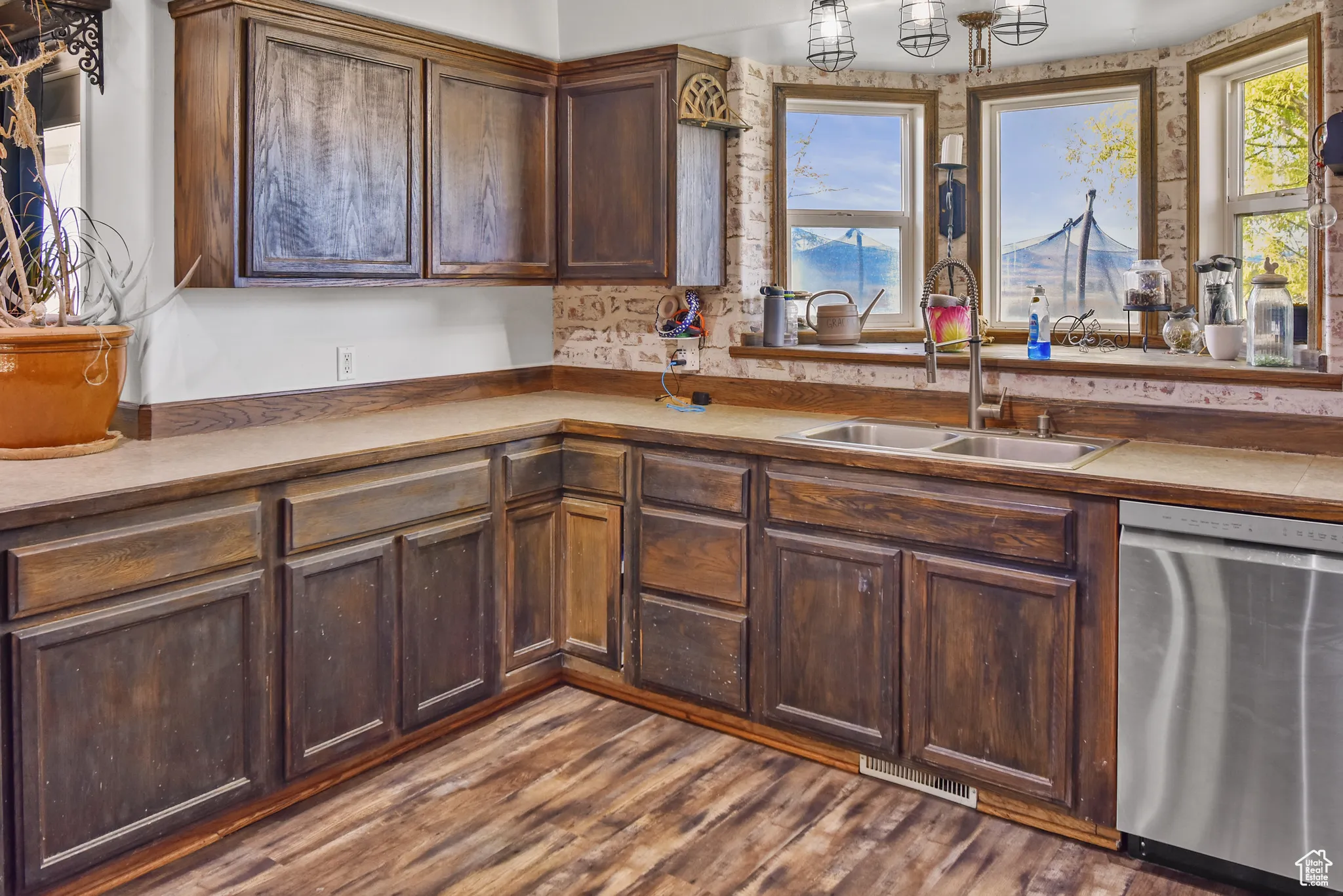 Kitchen featuring stainless steel dishwasher, dark brown cabinets, dark wood finished floors, and light countertops