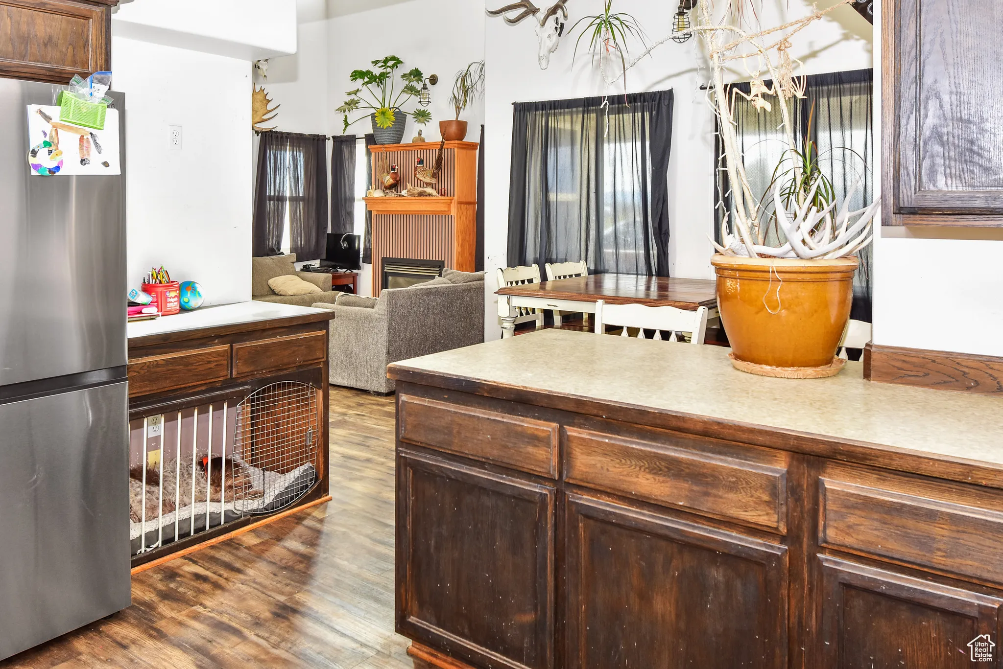 Kitchen featuring dark brown cabinets, freestanding refrigerator, a fireplace, dark wood-type flooring, and light countertops