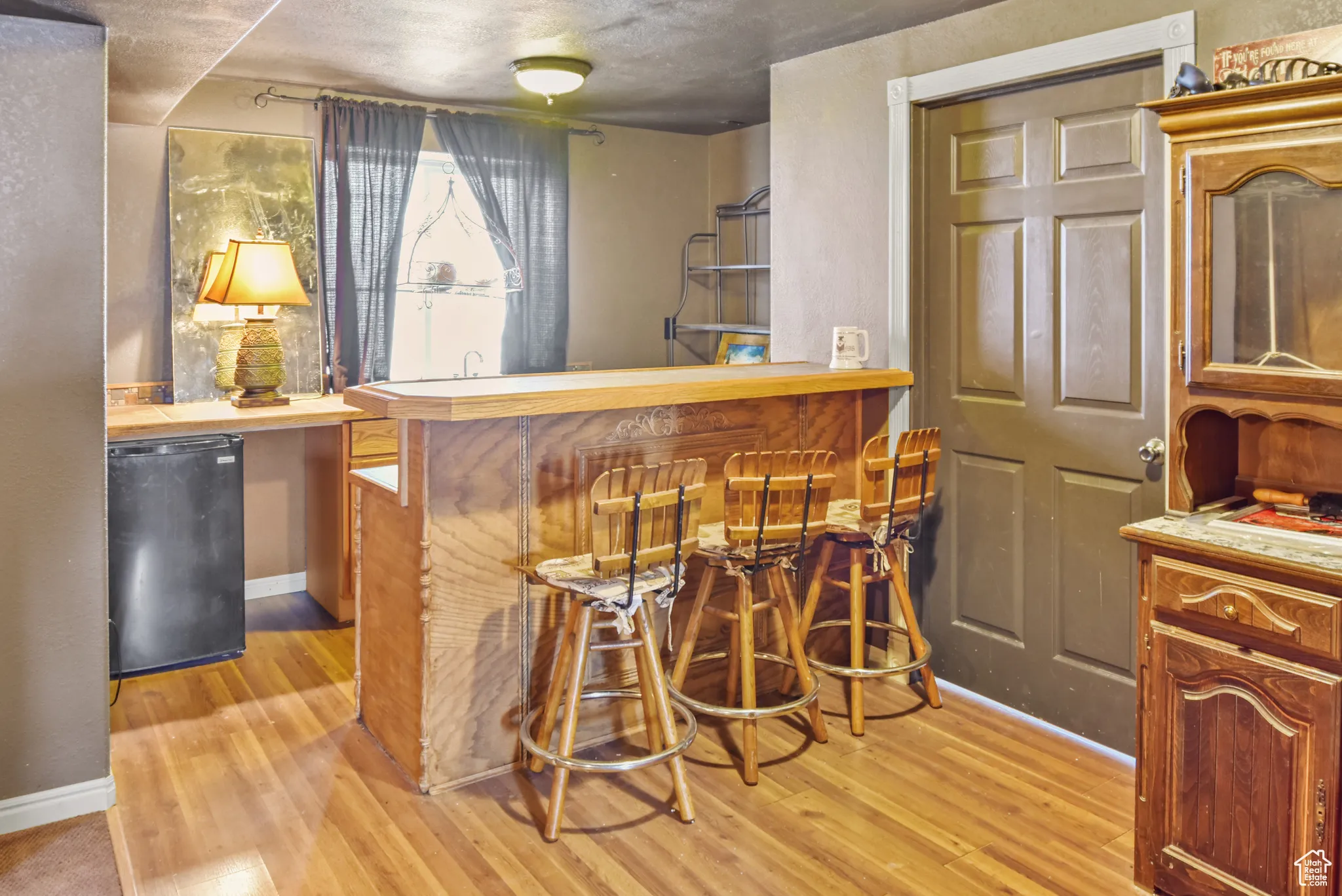 Indoor wet bar featuring light countertops, light wood finished floors, black fridge, and brown cabinets