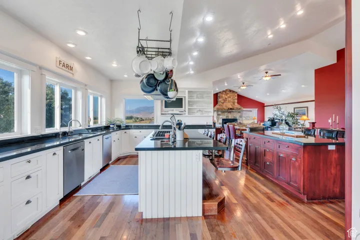 Kitchen featuring a center island with sink, light wood-type flooring, lofted ceiling, a stone fireplace, and open floor plan
