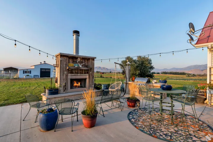 View of patio with outdoor dining space, a warm lit fireplace, area for grilling, a mountain view, and a view of rural / pastoral area