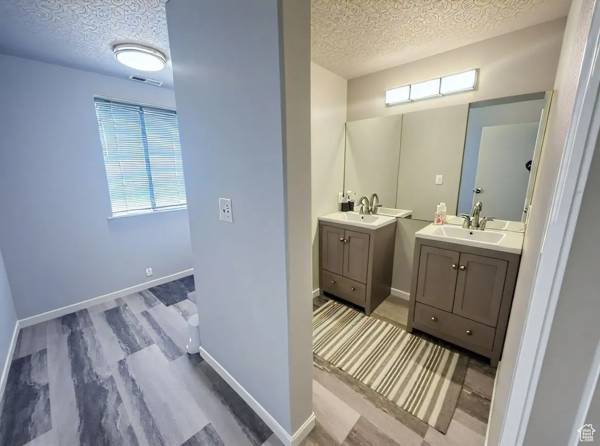 Bathroom featuring two vanities, light wood-style floors, and a textured ceiling
