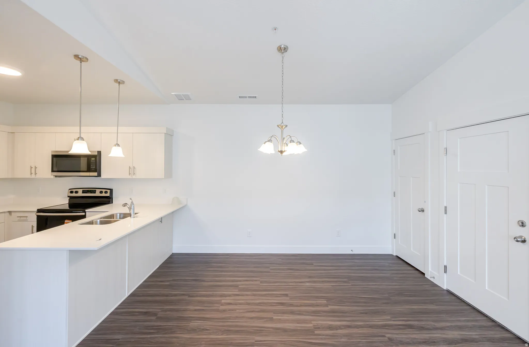 Kitchen featuring a peninsula, stainless steel appliances, white cabinetry, and dark wood-style flooring