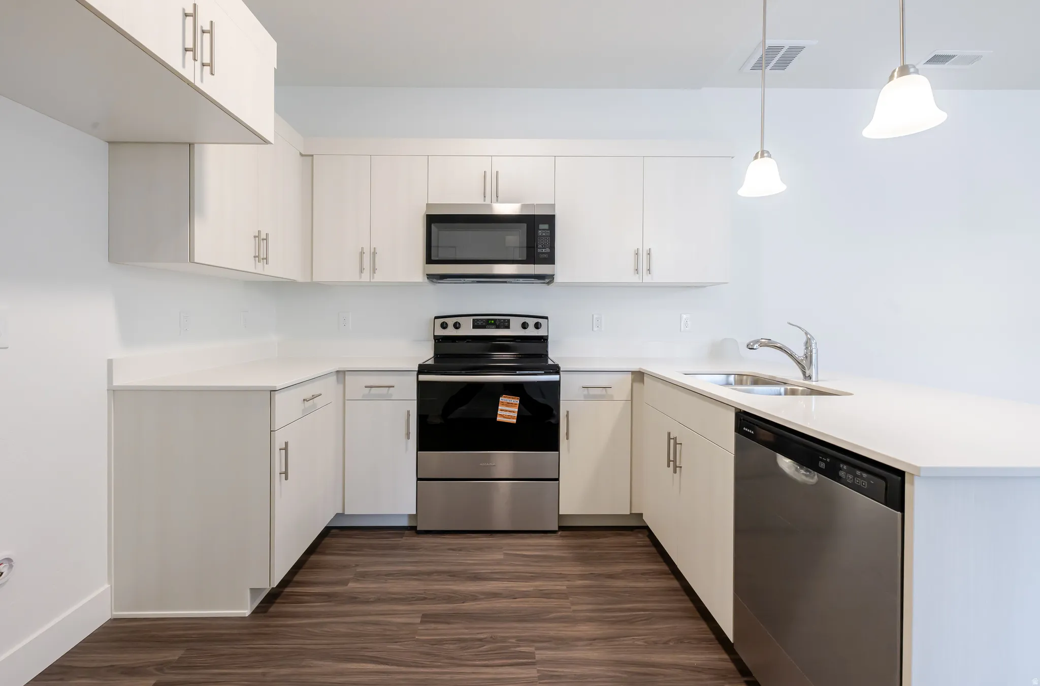 Kitchen with stainless steel appliances, a peninsula, dark wood-type flooring, hanging light fixtures, and white cabinets