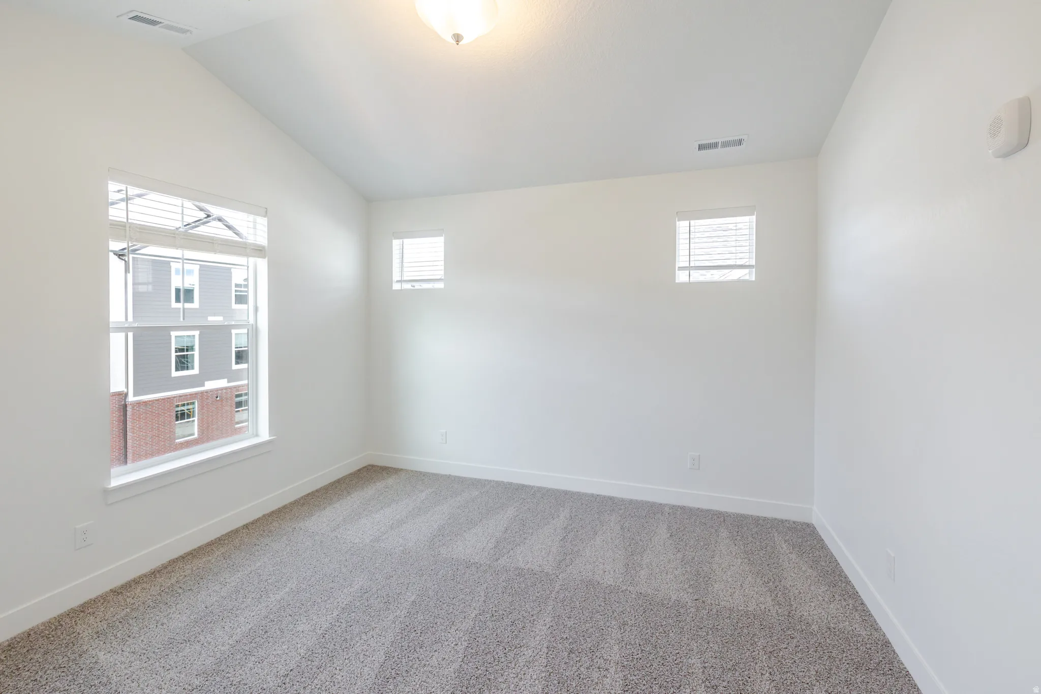 Empty room with light colored carpet, lofted ceiling, and plenty of natural light