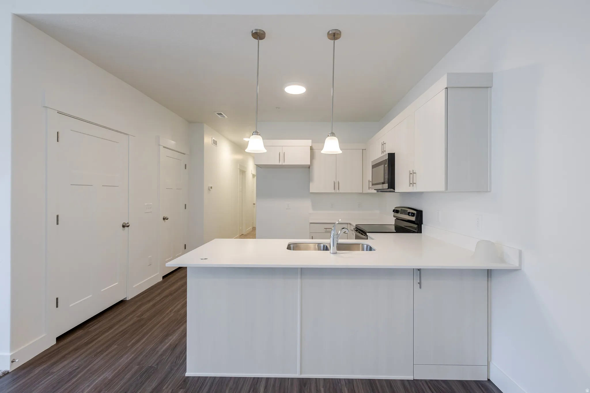 Kitchen featuring a peninsula, white cabinets, stainless steel appliances, dark wood finished floors, and hanging light fixtures