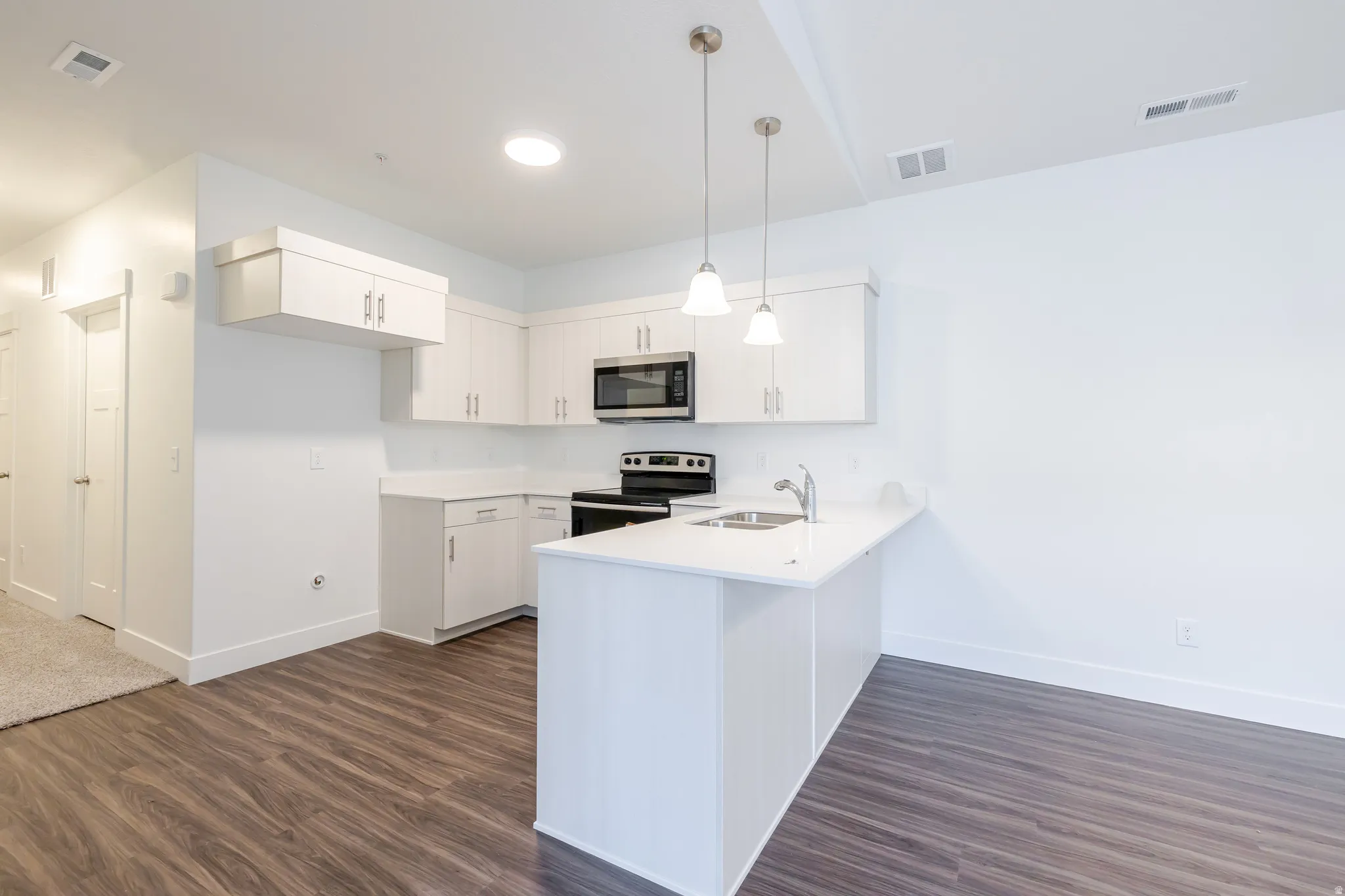 Kitchen with stainless steel appliances, a peninsula, dark wood finished floors, pendant lighting, and white cabinets