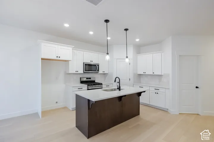 Modern kitchen featuring white cabinetry, a dark wood-finish island with a light-toned countertop, stainless steel appliances, and wood-finish flooring