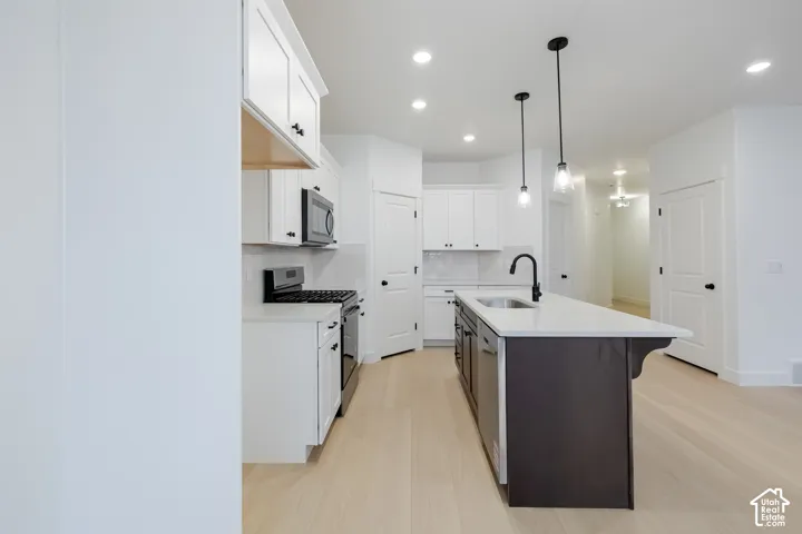 Kitchen featuring white cabinetry, dark-finish central island, stainless steel appliances, light-toned flooring, and pendant lighting