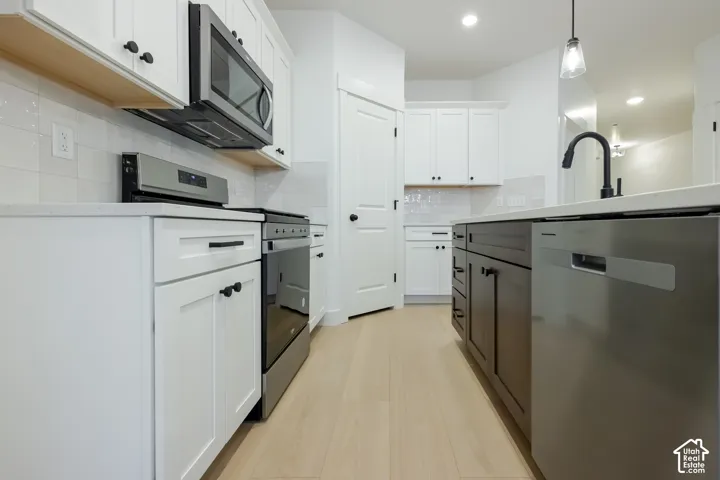 Contemporary kitchen featuring white cabinetry, light wood-finish flooring, stainless steel appliances, a kitchen island, and a tile backsplash