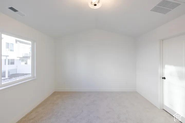 Vaulted ceiling with a flush-mount light fixture, white interior door with black hardware, and a window with white trim